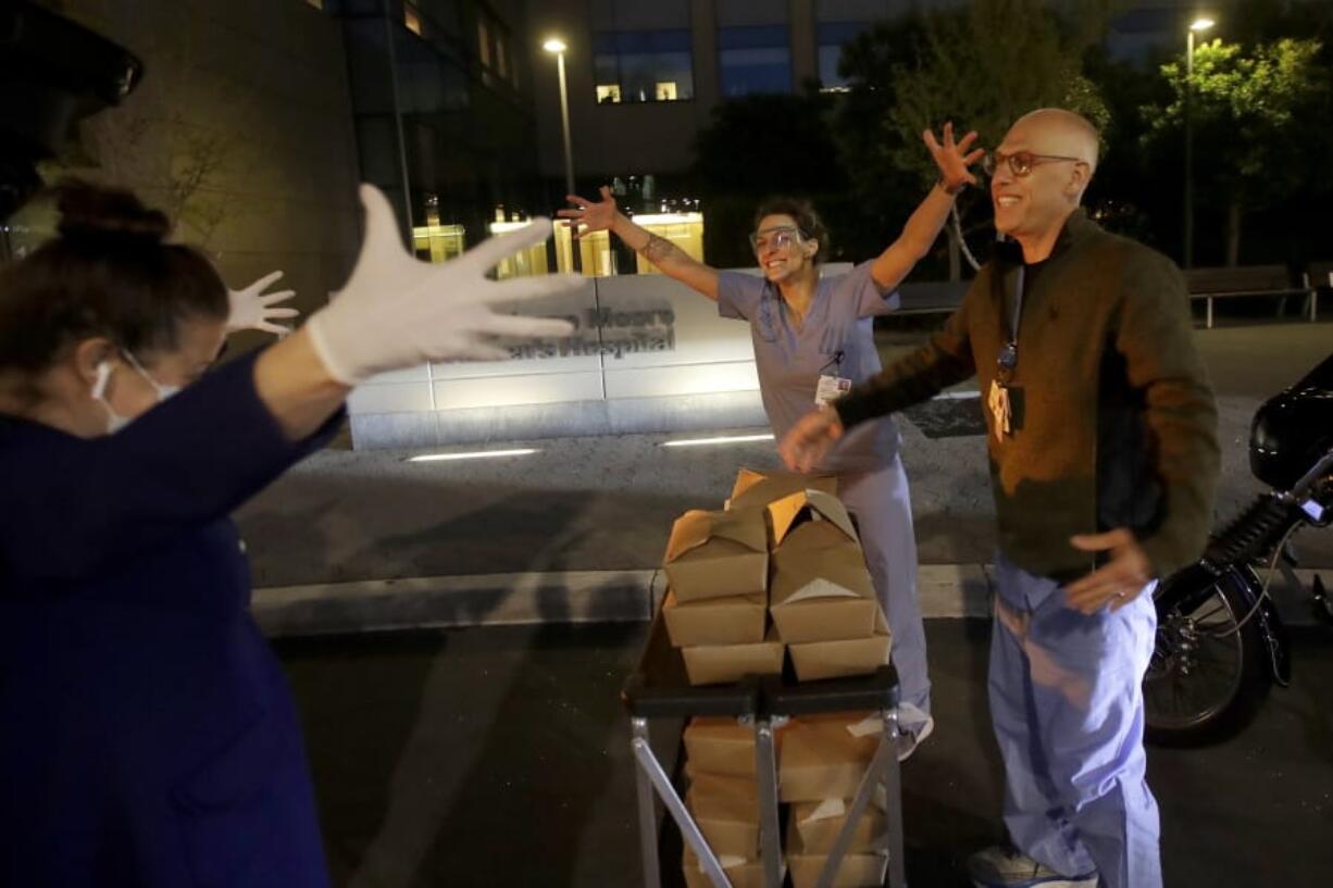 In this Friday, March 27, 2020, photo, Nightbird Restaurant chef and owner Kim Alter, left, mimicks giving a hug to nurse practitioner Sydney Gressel, center, and patient care technician Matt Phillips after delivering dinner to them at University of California at San Francisco Benioff Children&#039;s Hospital in San Francisco. A group of tech-savvy, entrepreneurial San Francisco friends wanted to help two groups devastated by the coronavirus pandemic. They came up with a plan that involved soliciting donations, tapping friends in the restaurant world and getting San Francisco hospitals to accept free food cooked up by some of the city&#039;s top chefs.