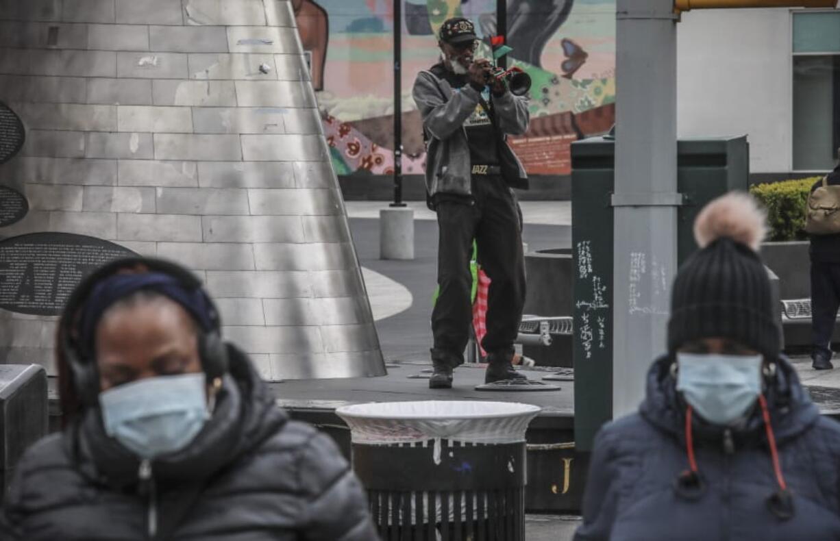 A familiar resident of Harlem who goes by the name New World Warrior, center, plays &quot;Lift Every Voice And Sing&quot; on his trumpet at one of multiple stops along 125th Street, blaring the song repeatedly as people walk on by Saturday April 18, 2020, in New York. &quot;I am not concerned about corona[virus],&quot; he said, &quot;I am concerned about the core of racism.&quot; On Friday, the Centers for Disease Control and Prevention released its first breakdown of COVID-19 case data by race, showing that 30% of patients whose race was known were black. The federal data was missing racial information for 75% of all cases, however, and did not include any demographic breakdown of deaths.