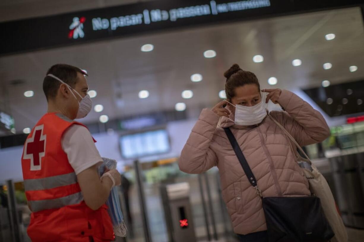 A passenger receives a face mask distributed by a red cross volunteer at the main train station in Barcelona, Spain, Tuesday, April 14, 2020. Face mask distribution in train and bus stations continue as factory and construction workers resume their activities in roughly half of Spanish regions emerging from the Easter holiday period. Spain&#039;s left-wing Cabinet is expected to pass new measures to aide smaller business and the self-employed affected by the freezing of economic activity.