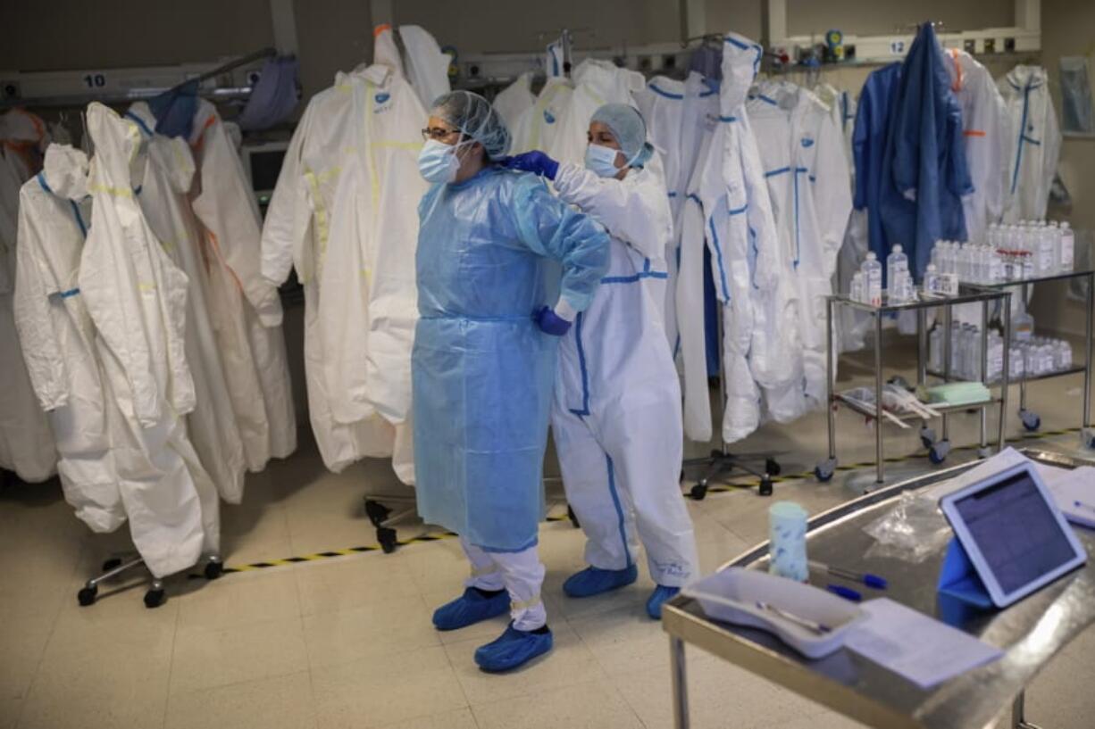 In this Thursday, April 16, 2020 photo, healthcare workers put on protective gear in order to assist a coronavirus patient at the intensive care unit (ICU) of the Clinica CEMTRO in Madrid, Spain.