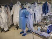 In this Thursday, April 16, 2020 photo, healthcare workers put on protective gear in order to assist a coronavirus patient at the intensive care unit (ICU) of the Clinica CEMTRO in Madrid, Spain.