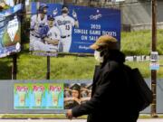 FILE - In this April 2, 2020, file photo, a pedestrian wears a hat and a face mask on Sunset Blvd., in the Echo Park neighborhood of Los Angeles. With no games being played, recent sports headlines have centered around hopes and dreams -- namely, the uncharted path leagues and teams must navigate to return to competition in the wake of the pandemic.