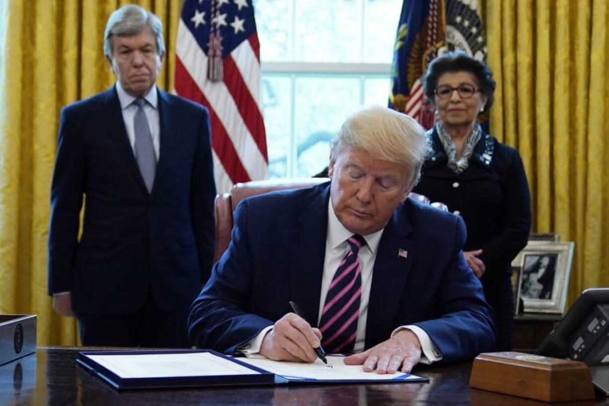 President Donald Trump signs a coronavirus aid package to direct funds to small businesses, hospitals, and testing, in the Oval Office of the White House, Friday, April 24, 2020, in Washington. Sen. Roy Blunt, R-Mo., left, and Jovita Carranza, administrator of the Small Business Administration look on.