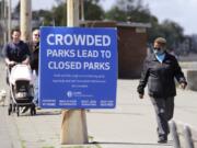 Velma Mullen, right, wears a protective mask as she walks past a sign advising park users to keep physical space between them Monday, April 27, 2020, in Seattle. City guidelines for Seattle parks ask that people stay at least six feet apart, not to congregate and to keep moving to help prevent spread of the coronavirus.