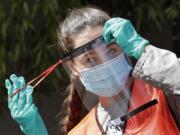 Volunteer Sarah Nishikawa tries on a homemade face shield to see how it works after receiving several shopping bags full of them at a drive-up donation location for medical supplies at the University of Washington to help fight the coronavirus outbreak Tuesday, April 14, 2020, in Seattle.