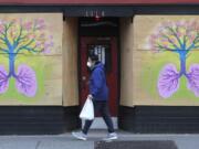 A pedestrian wearing a mask walks past paintings featuring lungs and a tree by Burgandy Viscosi on the boarded-up Re-Bar nightclub and theatre, Tuesday, April 14, 2020, in downtown Seattle. Streets and sidewalks in the area were quiet Tuesday as most people in the city are staying and working at home due to the outbreak of the coronavirus. (AP Photo/Ted S.