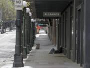 A person sleeps on the sidewalk near a closed AllSaints clothing store, Saturday, April 18, 2020, in downtown Seattle. Streets remained mostly empty due to Washington state&#039;s ongoing stay-at-home order and non-essential businesses continuing to be closed as a result of the outbreak of the coronavirus. (AP Photo/Ted S.