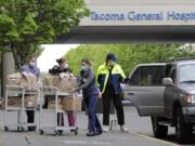 J.D. Elquist, right, of the Downtown Tacoma Partnership, delivers meals to workers at Tacoma General Hospital in Tacoma, Wash., Wednesday, April 29, 2020. The delivery was part of the organization's "Hero Meals" project, which collects donations from the public to purchase meals from restaurants that are then given to healthcare workers, first responders, and other essential workers in the city during the coronavirus outbreak. (AP Photo/Ted S.