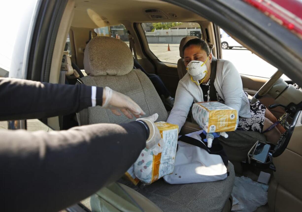 Mary Silva, left, with Pathways LA hands out diapers and hand sanitizers to Irma Juarez, who has two children ages 3 and 4, as Pathways LA and Hello Bello are distributing thousands of diapers to families in need April 14 as the coronavirus diaper shortage highlights tough choices for Los Angeles families.