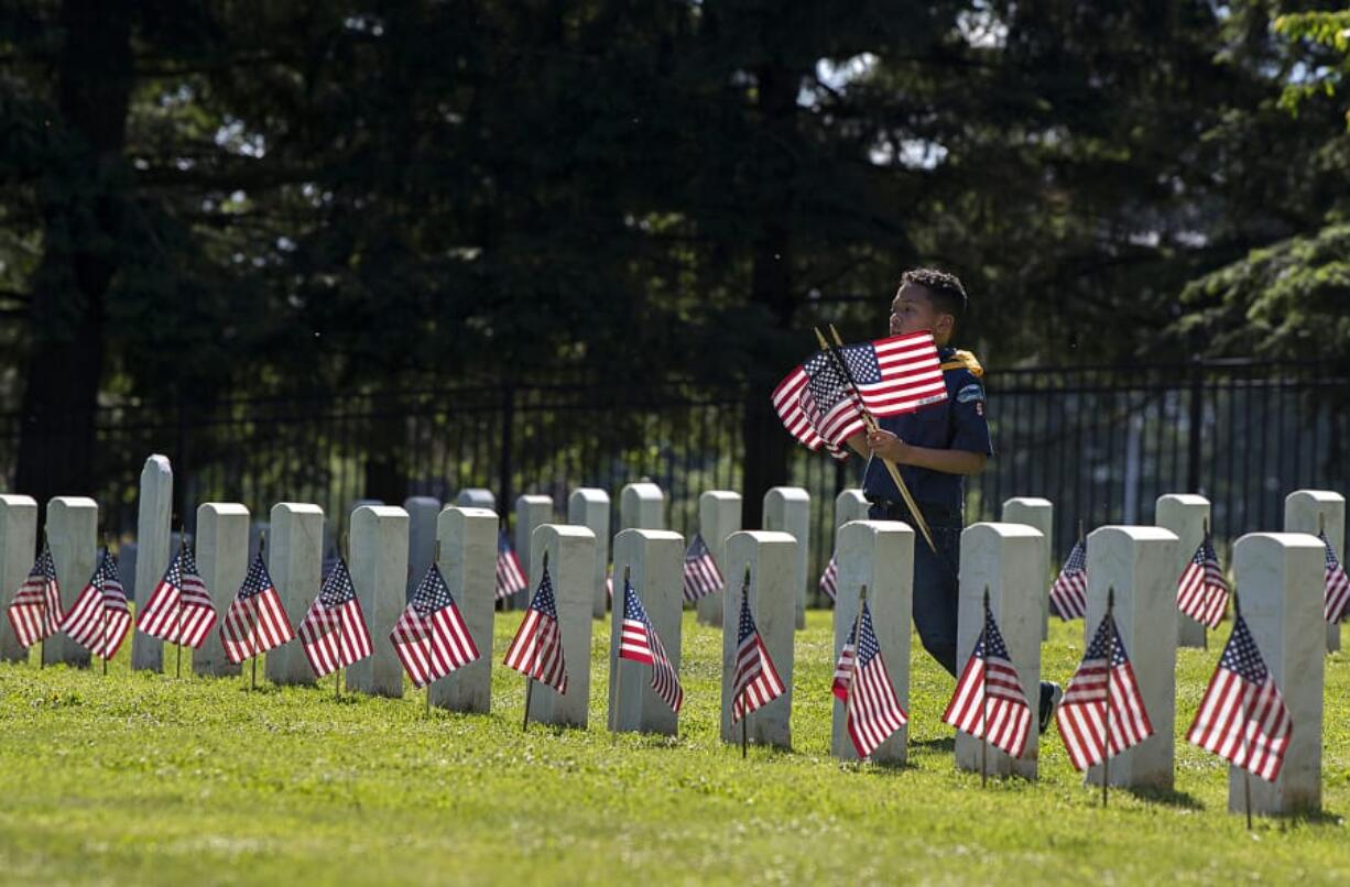 Savath Khieu, 8, of Vancouver, a member of Cub Scout Pack 9, helps honor soldiers at Vancouver Barracks National Cemetery on Thursday afternoon.