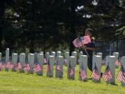 Savath Khieu, 8, of Vancouver, a member of Cub Scout Pack 9, helps honor soldiers at Vancouver Barracks National Cemetery on Thursday afternoon.