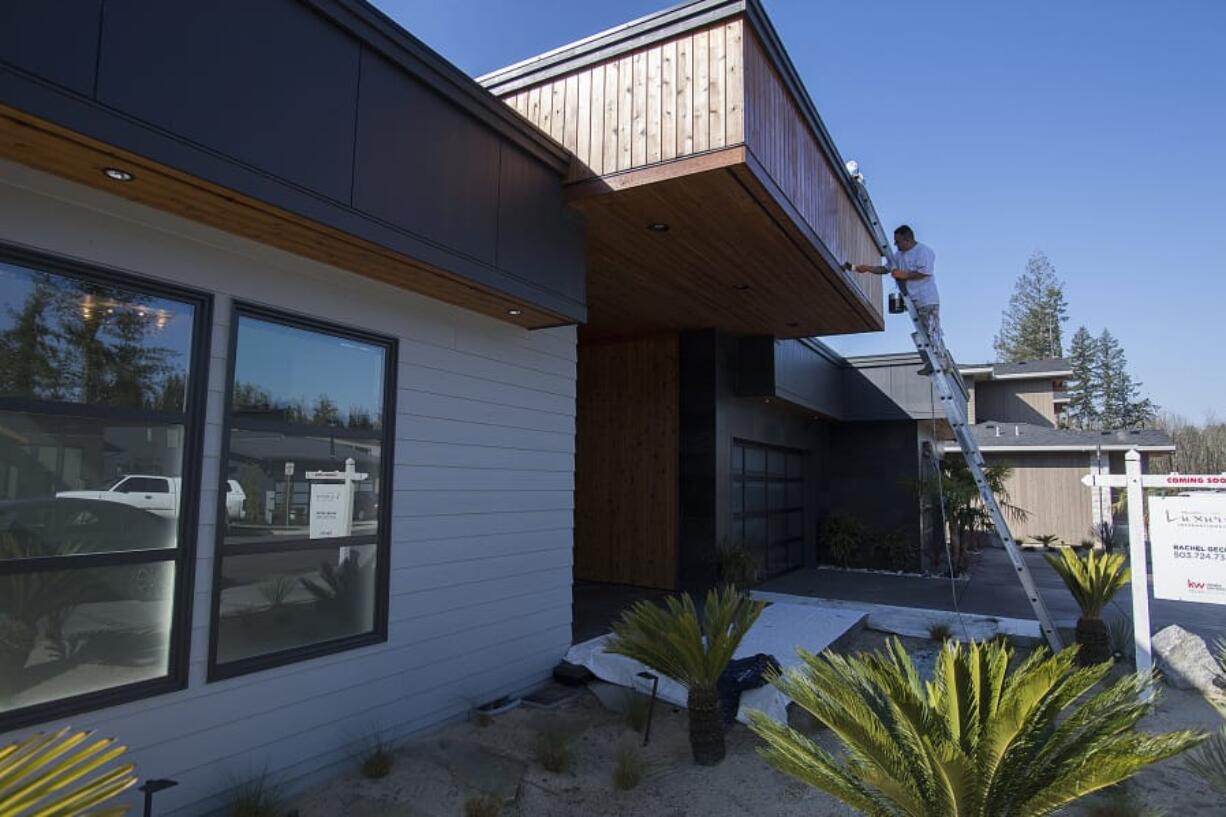 Jose Ramirez of Gecho Construction adds a fresh coat of stain to a new home at The Parklands in Camas in late March, as the impact of the novel coronavirus pandemic began to be felt. Home sales fell dramatically in the following month.