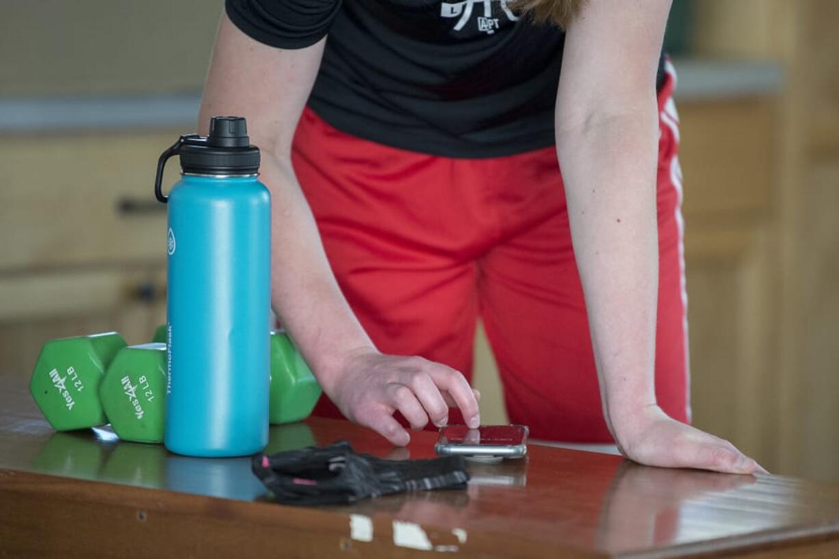 Faith Bergstrom of Camas gets instructions from her coach via smartphone as she works out in her family's garage during the COVID-19 pandemic Friday morning, May 8, 2020.