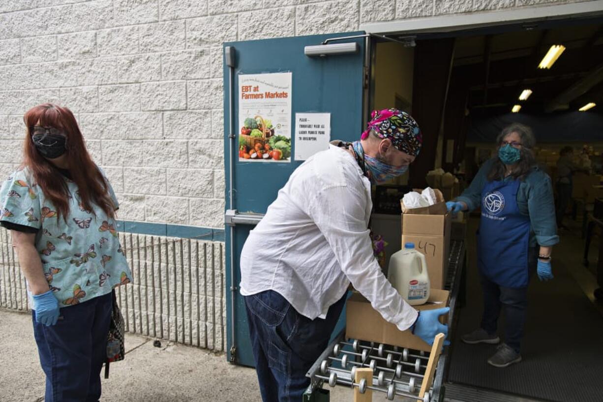 Elizabeth Bell, who works as an individual provider in Vancouver, from left, waits to pick up food for a client as Nicholas Chandler, also of Vancouver, picks up food off a conveyer belt with the help of volunteer Maggie Bomber of St. Vincent de Paul Vancouver on Thursday morning. St. Vincent de Paul Vancouver has been one of the busiest food pantries during the pandemic.