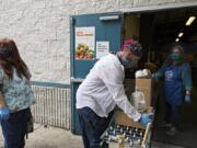 Elizabeth Bell, who works as an individual provider in Vancouver, from left, waits to pick up food for a client as Nicholas Chandler, also of Vancouver, picks up food off a conveyer belt with the help of volunteer Maggie Bomber of St. Vincent de Paul Vancouver on Thursday morning. St. Vincent de Paul Vancouver has been one of the busiest food pantries during the pandemic.