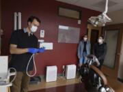 Justin Hollar, from left, of Oral Surgery Solutions in Vancouver demonstrates a new aerosol evacuator used in surgical procedures such as dental anesthesia, while assistant Elisa Spolar and oral surgery assistant Stephanie Biegler look on. Oral Surgery Solutions will operate at half its capacity for the time being to protect patients and staff from the novel coronavirus.