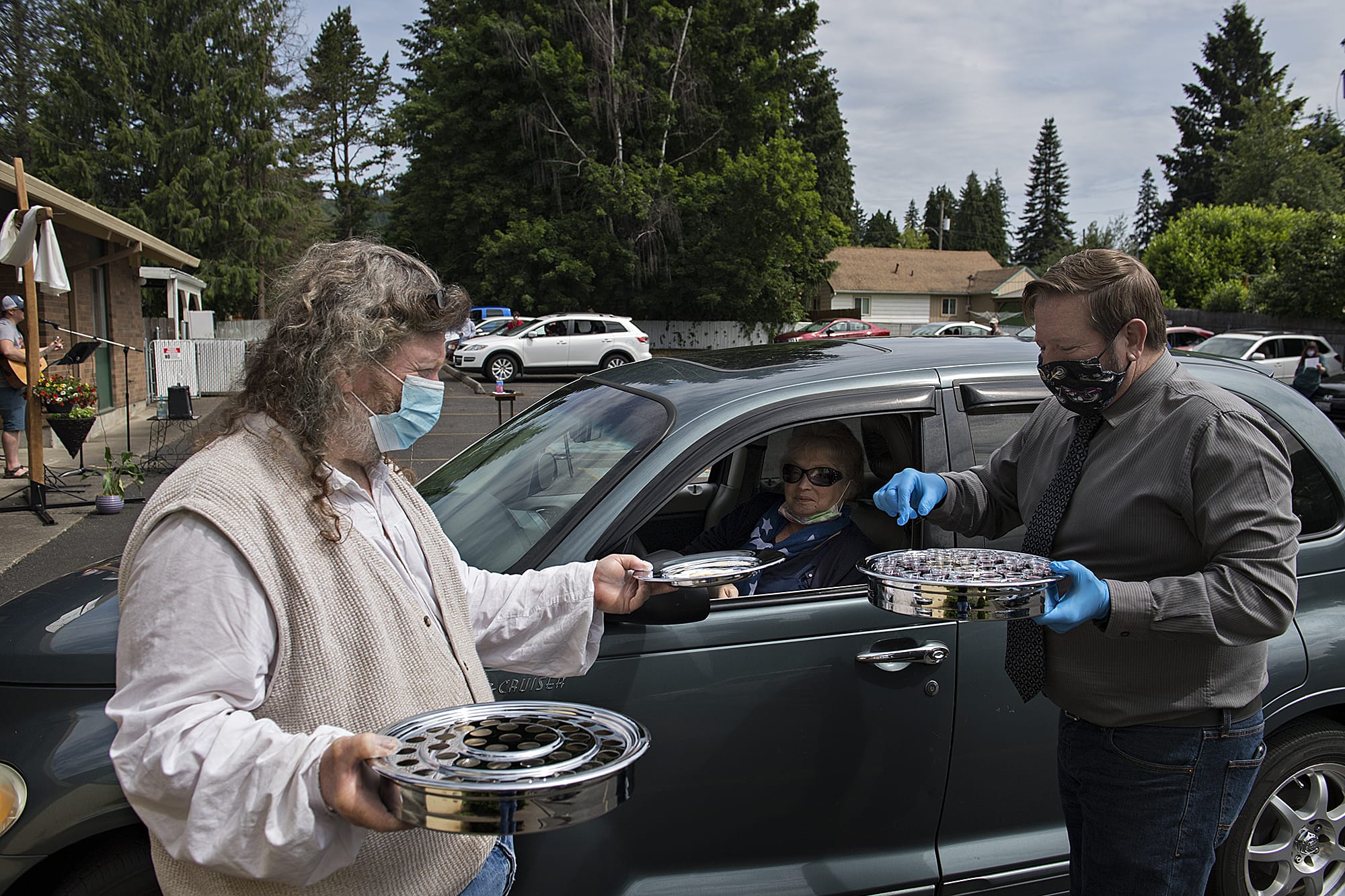 Charlie Raetz, left, a longtime member of St. Matthew Lutheran Church in Washougal, offers communion to Camas resident Tanya Fritz with the help of Pastor Robert Barber on Sunday morning, May 24, 2020. St. Matthew Lutheran Church, a small church in Washougal, offered its first drive-in church service that also included music, a message and cookies to-go for those in attendance.