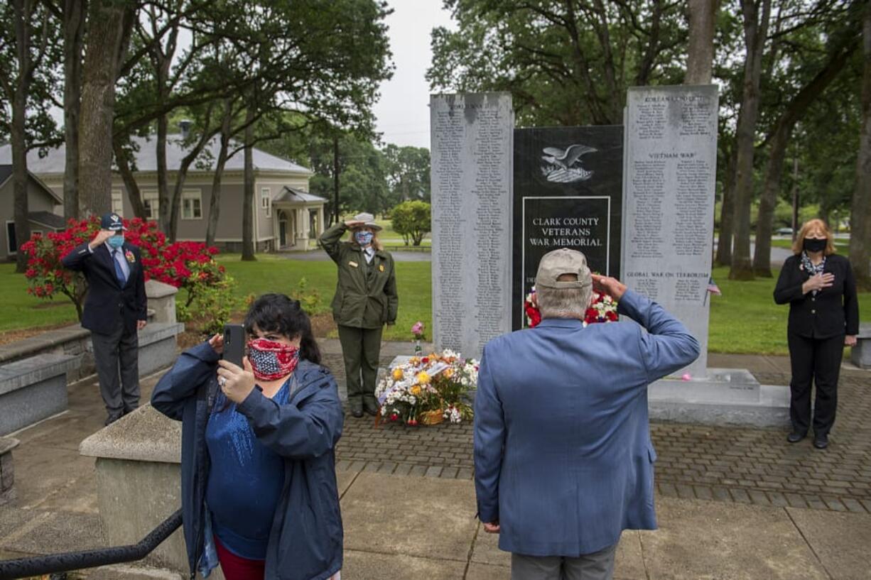 Veteran Marlene Varga of the Community Military Appreciation Committee, facing with phone, broadcasts a scaled-down version of the annual Memorial Day observance over Facebook live as taps is played at Fort Vancouver National Historic Site on Monday morning. Varga was joined by veteran Michael Burton, left, Fort Vancouver superintendent Tracy Fortmann, veteran Larry Smith and Mayor Anne McEnerny-Ogle. CMAC was not able to have its annual Memorial Day service because of COVID-19 concerns, so they hoped to share the experience over video. Varga said the holiday is not a day for a celebration but a day to remember those lost. &quot;We never forget,&quot; she said.