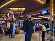 Security officer Stephen Henderson, center, wears a mask and gloves as he keeps an eye on the reopening while a thermometer, right, measures the temperature of guests at ilani Casino Resort on Thursday morning, May 28, 2020.