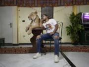 In this April 28, 2020 photo, 26-year-old lion tamer Ashraf el-Helw sits next to his 5-year-old female African lion &#039;Joumana,&#039; after preforming a show, part of a coronavirus stay home and stay safe call to encourage people to stay home, inside his family apartment, in Cairo, Egypt. With the national circus closed due to the pandemic el-Helw has his big cats performing tricks at his Cairo apartment and posts performance videos on social media.