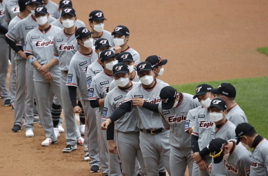 Hanwha Eagles players wearing face masks line up during the start of their regular season baseball game against SK Wyverns in Incheon, South Korea, Tuesday, May 5, 2020. Cheerleaders danced beneath rows of empty seats and umpires wore protective masks as a new baseball season began in South Korea. After a weeks-long delay because of the coronavirus pandemic, a hushed atmosphere allowed for sounds like the ball hitting the catcher&#039;s mitt and bats smacking the ball for a single or double to echo around the stadium.