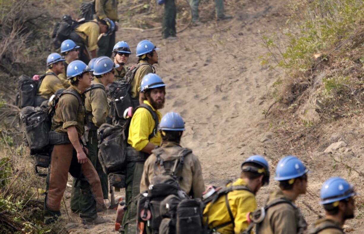 Firefighters watch Aug. 27, 2015, as a wildfire creeps toward their fire break near Chelan. Newly released national plans for fighting wildfires during the coronavirus pandemic are hundreds of pages long but don&#039;t offer many details on how fire managers will get access to COVID-19 tests or exactly who will decide when a crew needs to enter quarantine.