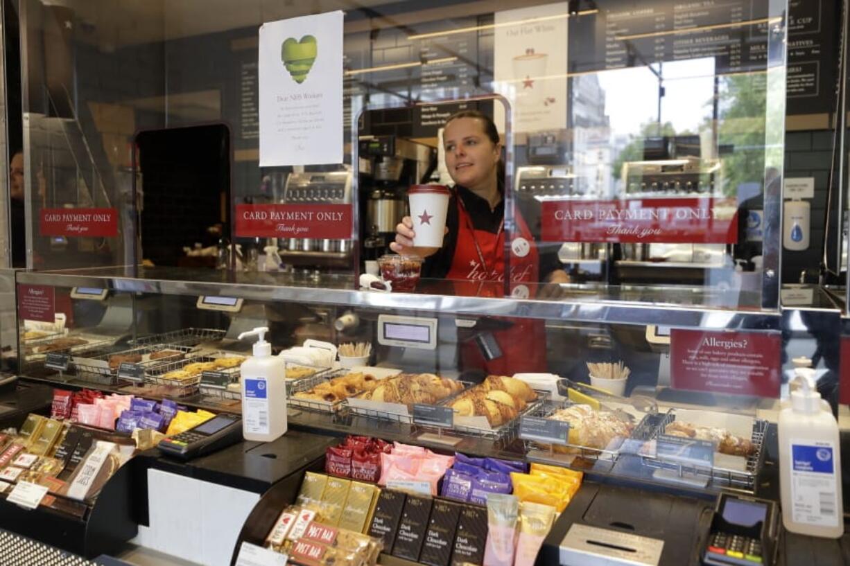 A barista serves from behind protective screens in a Pret coffee shop in London, Thursday, May 14, 2020, as the country continues in lockdown to help stop the spread of coronavirus, Some of the coronavirus lockdown measures are being relaxed in England, with coffee shops reopening but with extra measures such as take away only and social distancing.