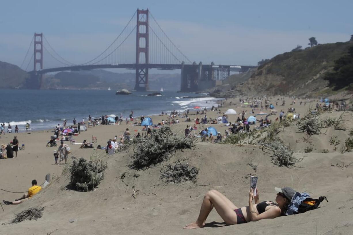 Sara Stewart, foreground, reads a book while away from crowds visiting Baker Beach during the coronavirus outbreak in San Francisco, Sunday, May 24, 2020.