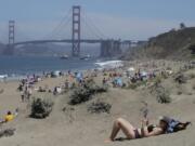 Sara Stewart, foreground, reads a book while away from crowds visiting Baker Beach during the coronavirus outbreak in San Francisco, Sunday, May 24, 2020.