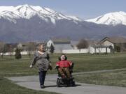 In this April 14, 2020, photo, Jodi Hansen walks with her son Jacob Hansen near their home, in Eagle Mountain, Utah. Even before the new coronavirus hit, cystic fibrosis meant a cold could put Jacob Hansen in the hospital for weeks. He relies on hand sanitizer and disinfecting wipes to keep germs at bay because has cerebral palsy and uses a wheelchair, but these days shelves are often bare. For millions of disabled people and their families, the coronavirus crisis has piled on new difficulties and ramped up those that already existed.