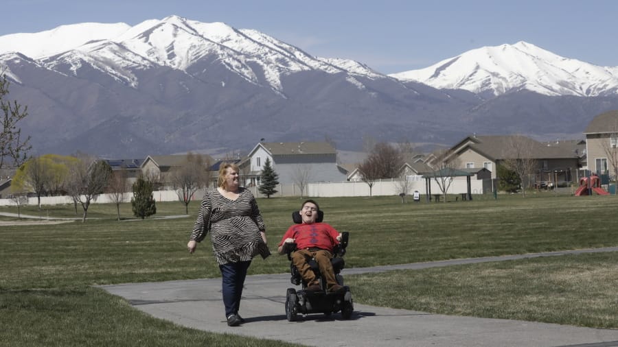 In this April 14, 2020, photo, Jodi Hansen walks with her son Jacob Hansen near their home, in Eagle Mountain, Utah. Even before the new coronavirus hit, cystic fibrosis meant a cold could put Jacob Hansen in the hospital for weeks. He relies on hand sanitizer and disinfecting wipes to keep germs at bay because has cerebral palsy and uses a wheelchair, but these days shelves are often bare. For millions of disabled people and their families, the coronavirus crisis has piled on new difficulties and ramped up those that already existed.