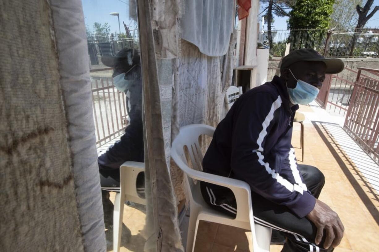 In this photo taken on Monday, April 27, 2020, a man sits outside an house where 46 men, from Nigeria and Ghana live in Castel Volturno, near Naples, Southern Italy. The house has no running water, the dilapidated electrical system doesn&#039;t reach many rooms that are in the dark. They are known as &quot;the invisibles,&quot; the undocumented African migrants who, even before the coronavirus outbreak plunged Italy into crisis, barely scraped by as day laborers, prostitutes and seasonal farm hands. Locked down for two months in their overcrowded apartments, their hand-to-mouth existence has grown even more precarious with no work, no food and no hope.