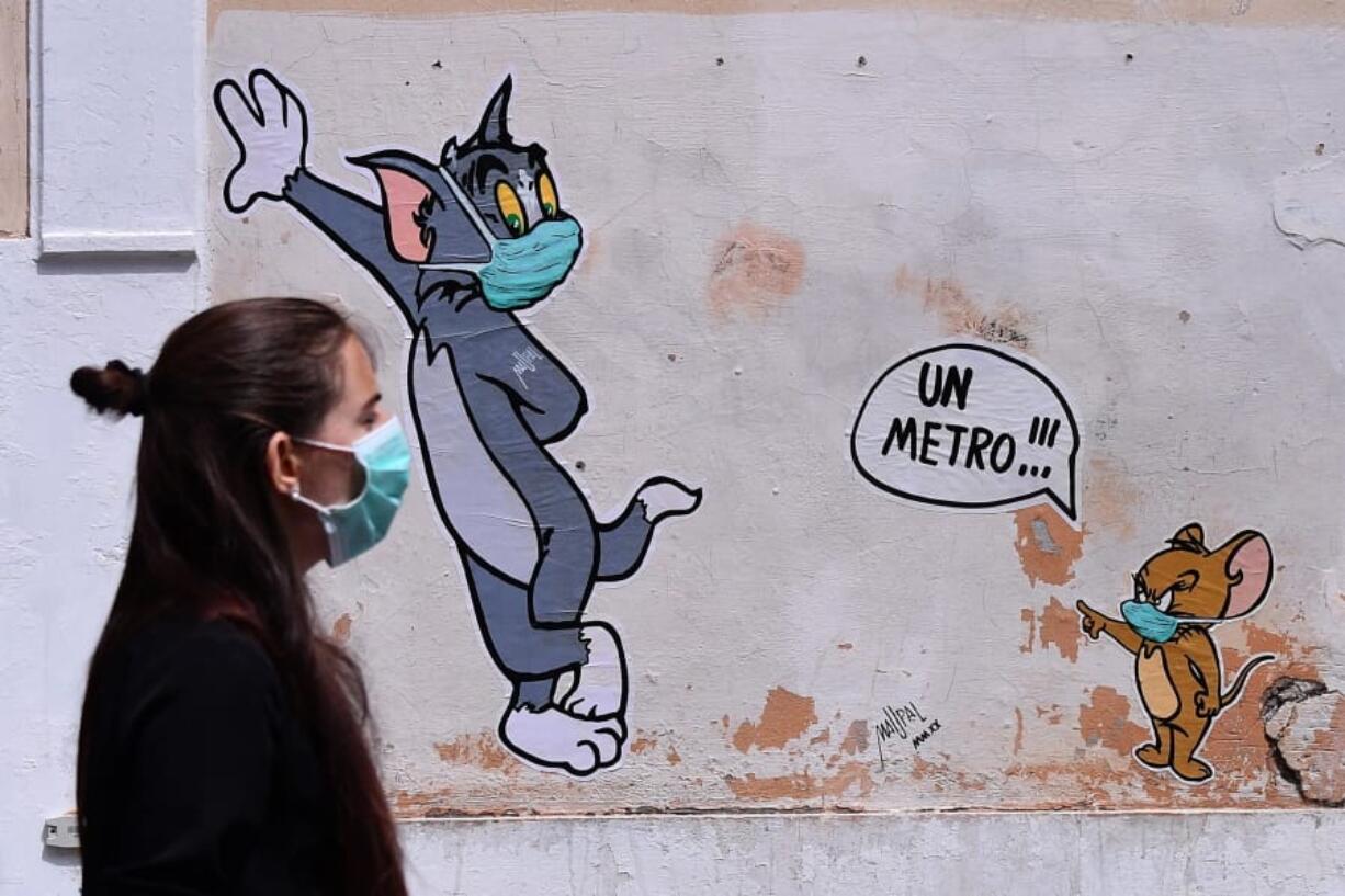 A woman wearing a face mask passes by a mural featuring William Hanna and Joseph Barbera&#039; s characters Tom &amp; Jerry mentioning the safe distance to be held from each other - &quot;One meter&quot; - in Rome, Friday, May 15, 2020. Italy is slowly reopening after the lockdown to prevent further spreading of COVID-19.