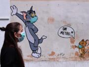 A woman wearing a face mask passes by a mural featuring William Hanna and Joseph Barbera&#039; s characters Tom &amp; Jerry mentioning the safe distance to be held from each other - &quot;One meter&quot; - in Rome, Friday, May 15, 2020. Italy is slowly reopening after the lockdown to prevent further spreading of COVID-19.