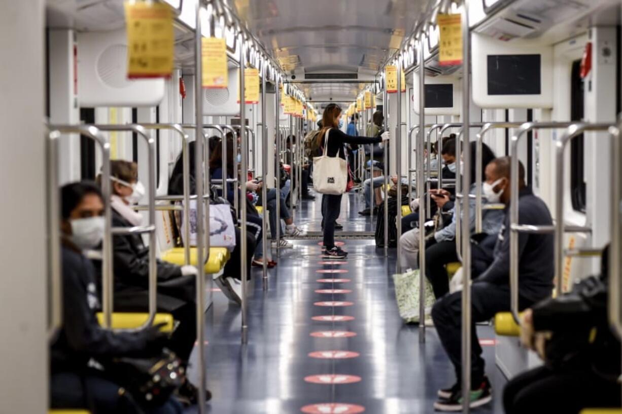 Commuters sit in the subway in Milan, Italy, Monday, May 4, 2020.  Marks on the floor show the correct distance to be kept. Italy began stirring again Monday after a two-month coronavirus shutdown, with 4.4 million Italians able to return to work and restrictions on movement eased in the first European country to lock down in a bid to stem COVID-19 infections.