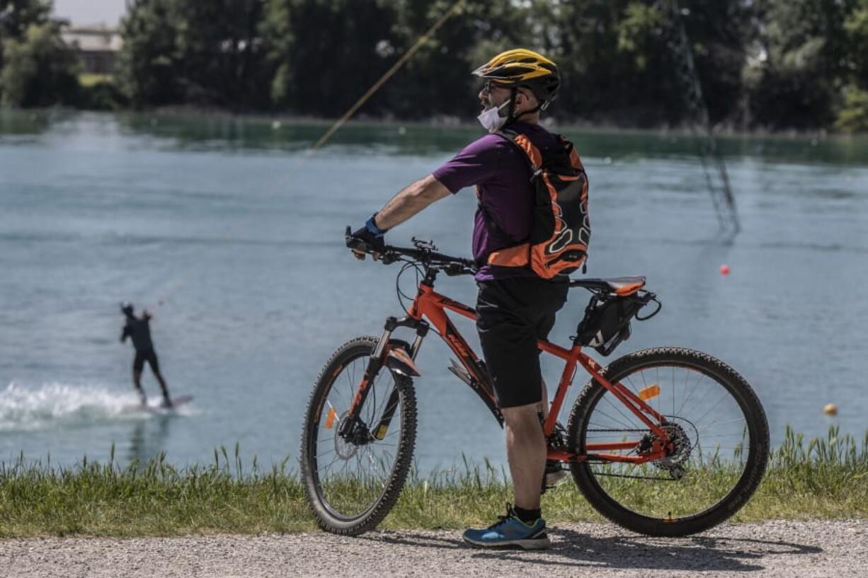 A man looks on his bike as another practices wakeboard at the Idroscalo artificial lake, in Milan, Italy, Saturday May, 9, 2020 following the loosening of a nationwide lockdown measure to prevent the spread of COVID-19.