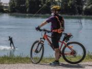 A man looks on his bike as another practices wakeboard at the Idroscalo artificial lake, in Milan, Italy, Saturday May, 9, 2020 following the loosening of a nationwide lockdown measure to prevent the spread of COVID-19.