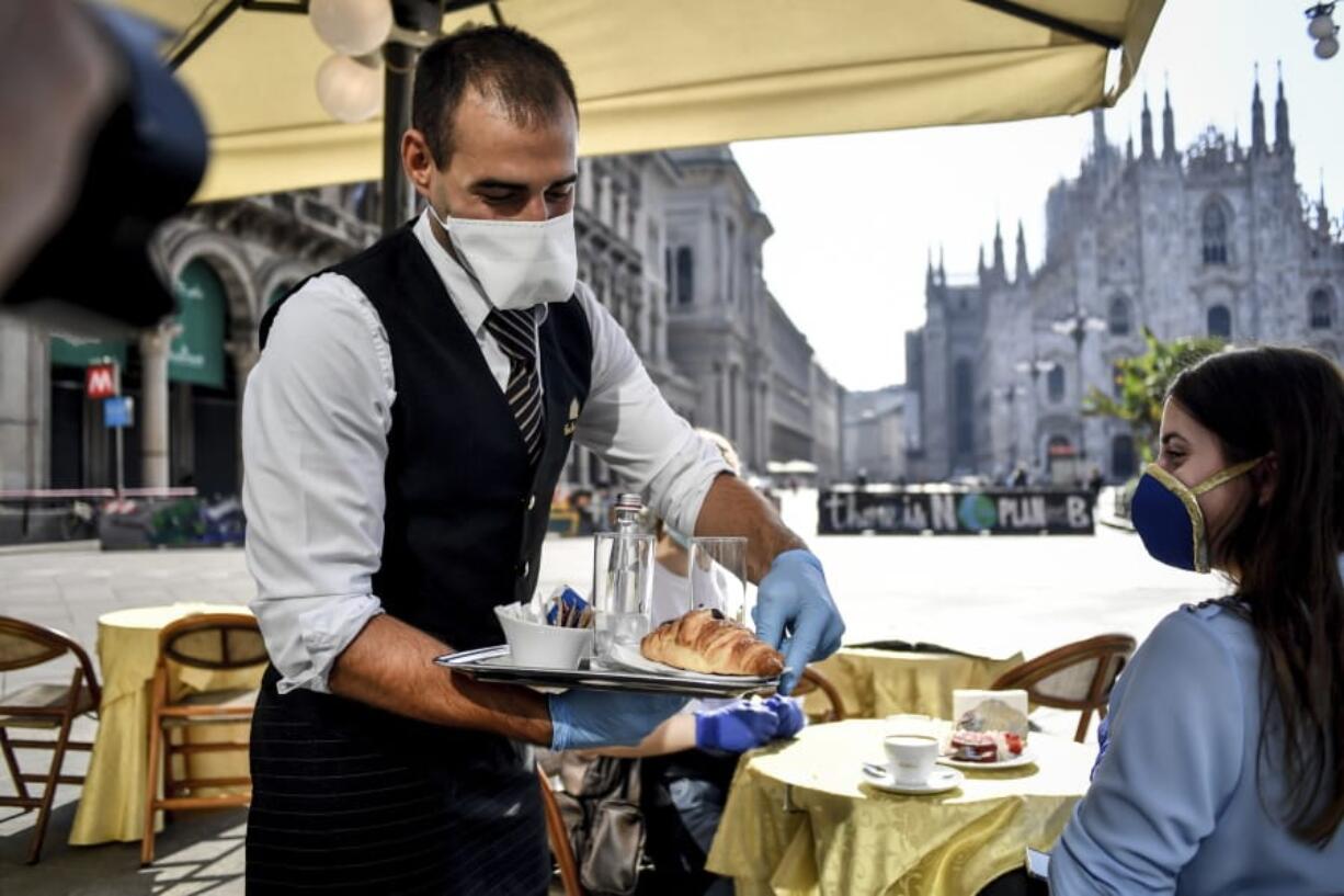 Two girls have breakfast served at a bar in front of the gothic Cathedral in Milan, Italy, Monday, May 18, 2020. Italy is slowly lifting sanitary restrictions after a two-month coronavirus lockdown.