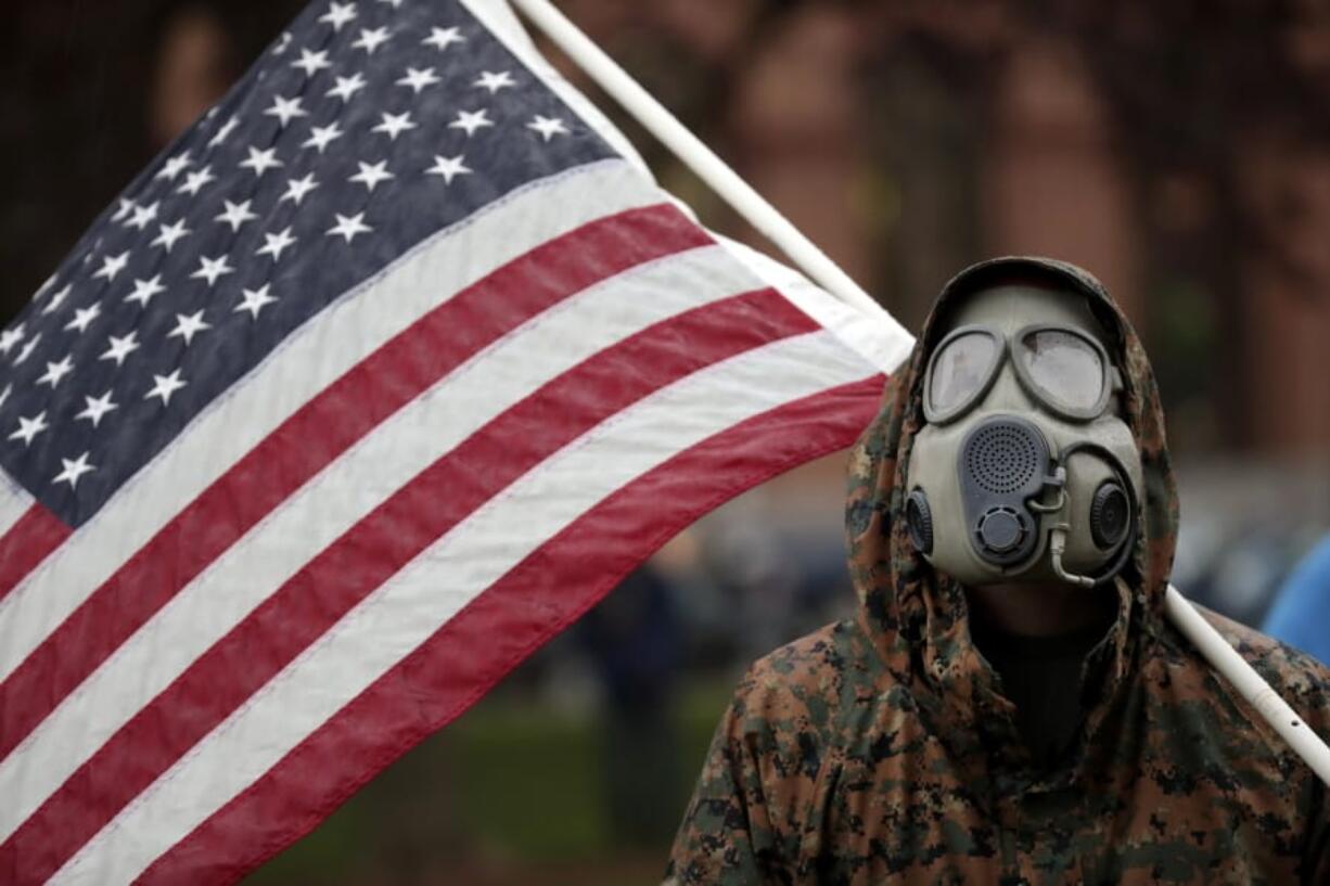 A protester wears a gas mask and carries an American flag during a rally in response to Michigan&#039;s coronavirus stay-at-home order at the State Capitol in Lansing, Mich., Thursday, May 14, 2020.