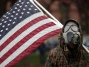 A protester wears a gas mask and carries an American flag during a rally in response to Michigan&#039;s coronavirus stay-at-home order at the State Capitol in Lansing, Mich., Thursday, May 14, 2020.