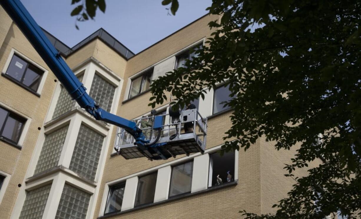 In this photo taken on Saturday, May 9, 2020, Eve Putseys, left, rides on a crane platform after visiting her deaf aunt, Suzanne Putseys, waving from her upper floor window at the La Cambre senior living home in Watermael-Boitsfort, Belgium. Tristan Van den Bosch, an operator of mobile platforms, saw his equipment stand idle because of the coronavirus pandemic and realized too many families could not see their locked-up elderly in care homes. Two problems created one solution and Van den Bosch has been driving his cranes to care homes in several towns across Belgium to lift the spirits of all involved.