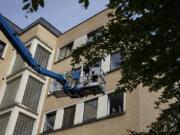 In this photo taken on Saturday, May 9, 2020, Eve Putseys, left, rides on a crane platform after visiting her deaf aunt, Suzanne Putseys, waving from her upper floor window at the La Cambre senior living home in Watermael-Boitsfort, Belgium. Tristan Van den Bosch, an operator of mobile platforms, saw his equipment stand idle because of the coronavirus pandemic and realized too many families could not see their locked-up elderly in care homes. Two problems created one solution and Van den Bosch has been driving his cranes to care homes in several towns across Belgium to lift the spirits of all involved.