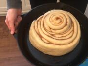 In this April 11, 2020 image from video provided by Whitney Rutz, Whitney Rutz displays a large cinnamon roll before putting it in the oven in her home in Portland, Ore. Rutz baked cinnamon rolls to help raise funds for Oregon Food Bank.