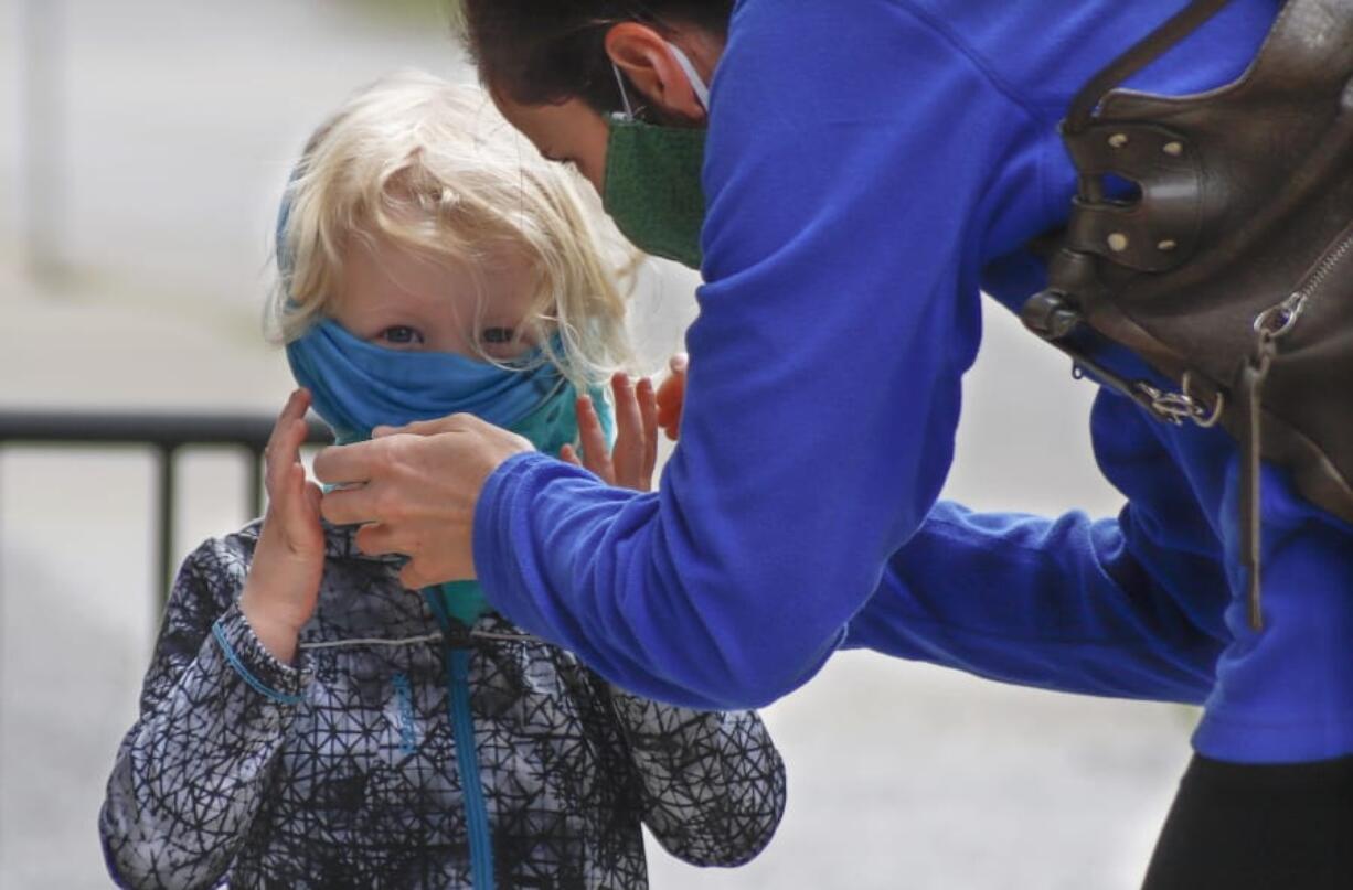 Bridget Kreider, right, helps her three-year-old daughter Maggie pull on her protective face covering before entering a store, Wednesday, May 20, 2020, in Harmony, Pa. Customers entering stores are required to wear face coverings to help prevent the spread of the new coronavirus during the COVID-19 pandemic under the state yellow phase reopening guide.