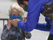 Bridget Kreider, right, helps her three-year-old daughter Maggie pull on her protective face covering before entering a store, Wednesday, May 20, 2020, in Harmony, Pa. Customers entering stores are required to wear face coverings to help prevent the spread of the new coronavirus during the COVID-19 pandemic under the state yellow phase reopening guide.