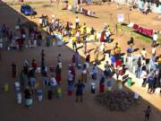 In this April, 24, 2020, photo, people wait to fetch water from a row of communal taps that the group Doctors Without Borders provided in a suburb of Harare, Zimbabwe. For people around the world who are affected by war and poverty, the simple act of washing hands is a luxury. In Zimbabwe, clean water is often saved for daily tasks like doing dishes and flushing toilets.