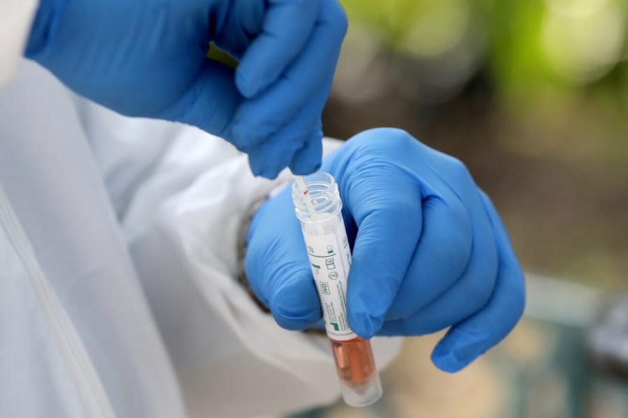 FILE - In this April 16, 2020, file photo, a medical worker places a swab in a vial while testing the homeless for COVID-19 through the Miami-Dade County Homeless Trust, during the new coronavirus pandemic, in Miami. An Associated Press analysis finds that most states are not meeting the minimum levels of testing suggested by the federal government and recommended by public health researchers even as many of them begin to reopen their shattered economies.