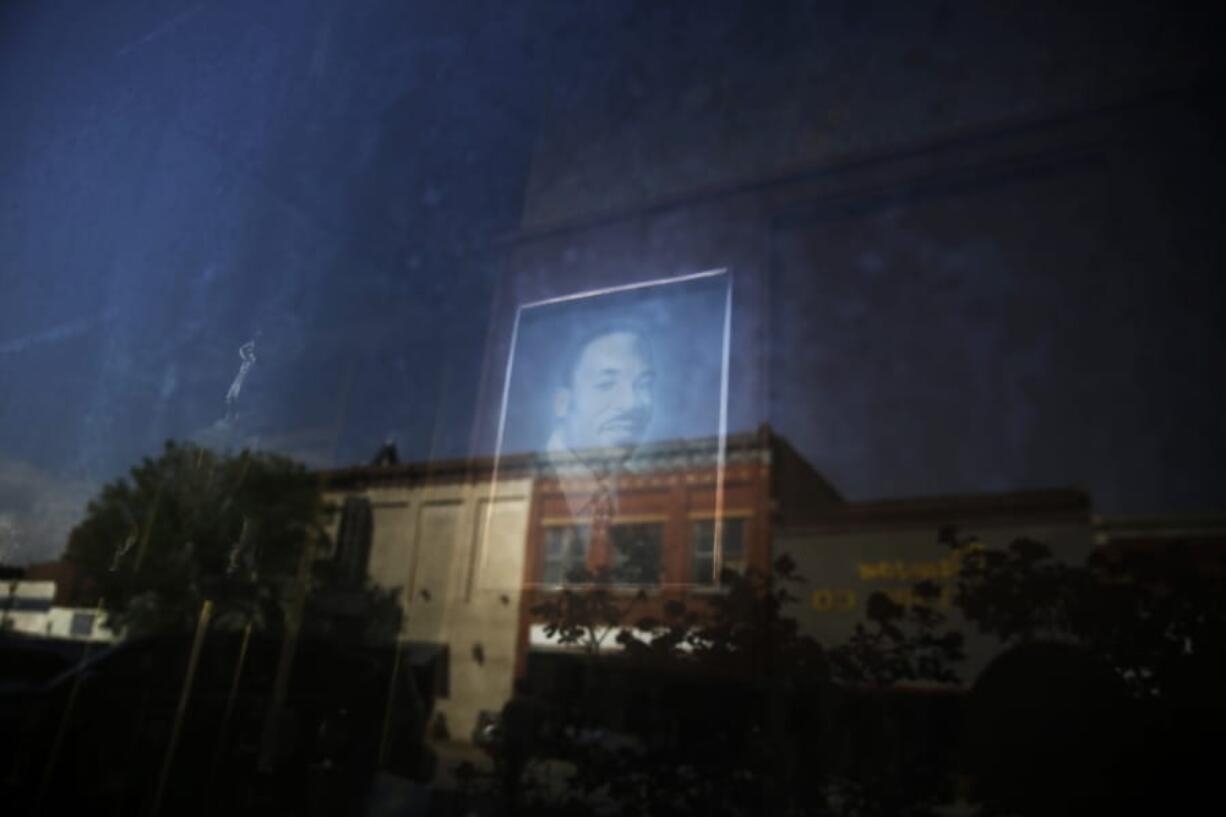 Downtown Dawson, Ga., is reflected in the window of a local barber shop where a photograph of Martin Luther King Jr. is on display on Friday, April 17, 2020. Across the county, as this state and others rush to throw open the doors on restaurants and stores, those here describe themselves as a cautionary tale of what happens when the virus seeps into American&#039;s most vulnerable communities, quietly at first then with breathtaking savagery.