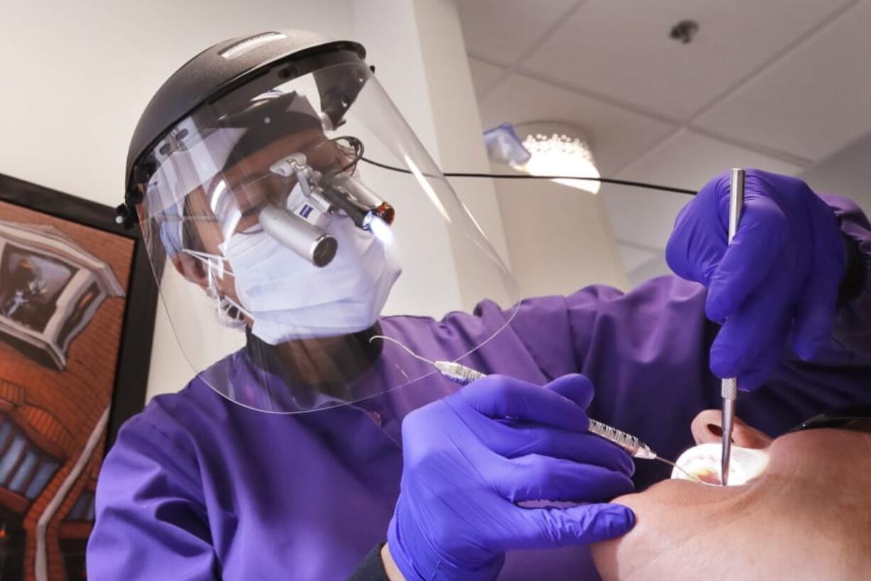 In this Wednesday, May 27, 2020 photo, dentist Dr. Kathleen Saturay wears additional protective equipment, including a face shield and disposable mask over a respirator mask, as she exams a patient in Seattle. Dental practices were allowed to open earlier this month following closure because of the coronavirus outbreak, as long as offices have enough personal protective equipment (PPE) for their staffers, put in place social-distancing policies and check patients for symptoms of COVID-19.