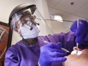 In this Wednesday, May 27, 2020 photo, dentist Dr. Kathleen Saturay wears additional protective equipment, including a face shield and disposable mask over a respirator mask, as she exams a patient in Seattle. Dental practices were allowed to open earlier this month following closure because of the coronavirus outbreak, as long as offices have enough personal protective equipment (PPE) for their staffers, put in place social-distancing policies and check patients for symptoms of COVID-19.